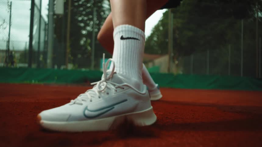 A tennis player's feet slide across a red clay court in a dynamic slow-motion close-up