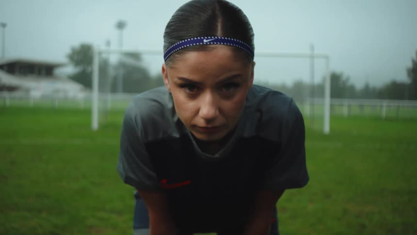 A determined female soccer player catches her breath on a rainy field and looks up with intensity in slow motion
