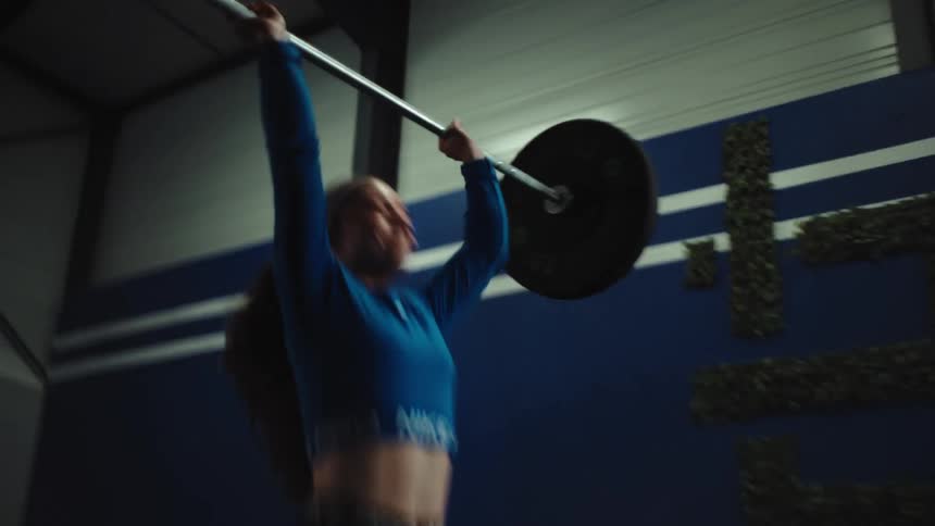 A determined female athlete successfully performs a powerful overhead press with a barbell in slow motion