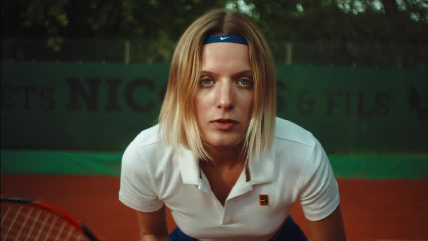 An intense female tennis player lifts her head in slow motion and stares down the camera, ready for the match