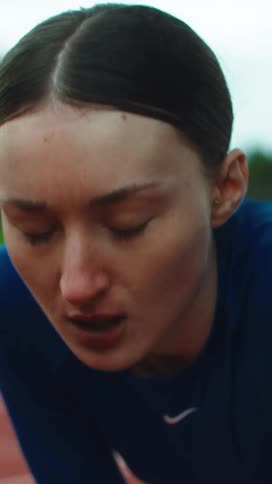 A determined female athlete takes a deep breath in a dramatic close-up, focusing intensely before a race on the track