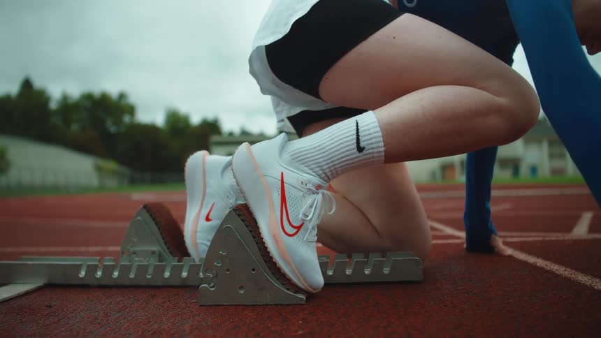 Close-up shot of a female athlete's feet in running shoes getting set in the starting blocks on a red track