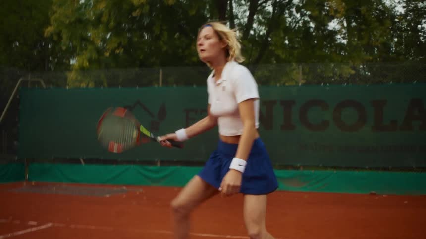 A determined female tennis player dressed in classic athletic wear volleys back and forth on a clay court