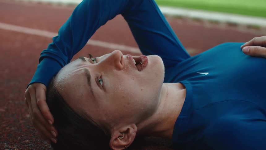 Close-up of an exhausted female runner catching her breath while lying on a stadium track after an intense workout