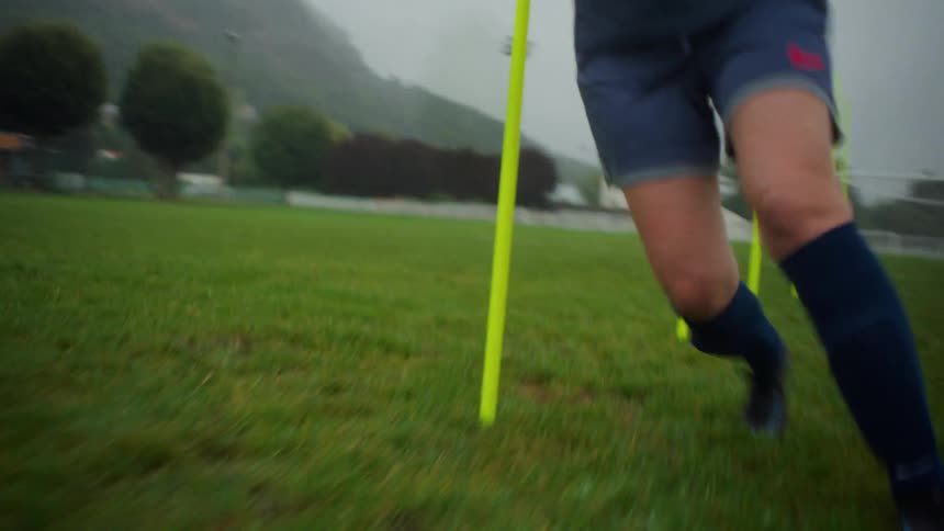 Close-up tracking shot of a female soccer player's quick footwork during agility pole drills on a foggy field