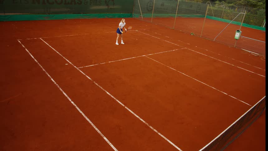High angle slow-motion view of a female tennis player executing a powerful serve on a red clay court