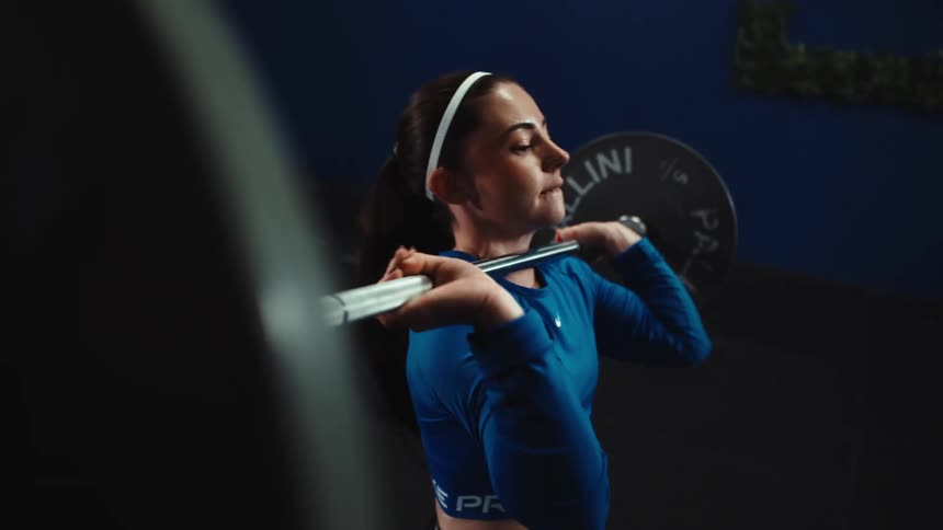 A determined female athlete completes a powerful clean lift with a barbell in a modern gym