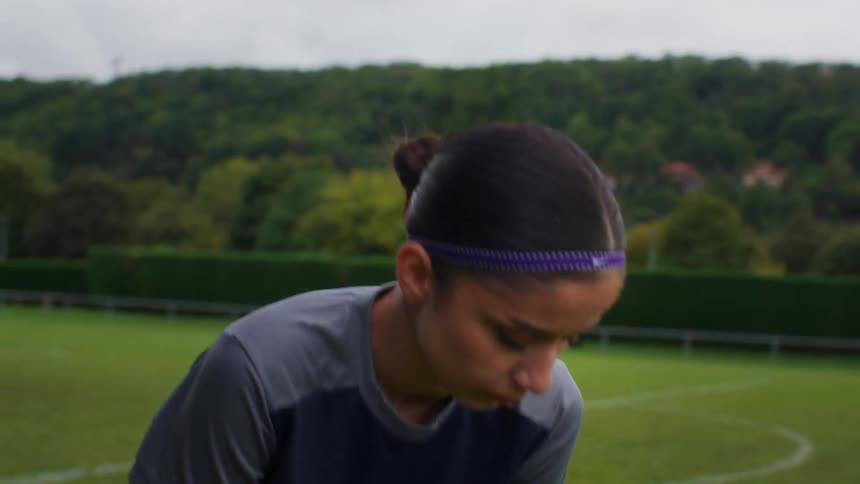 A tired female soccer player bends over to catch her breath on the field during practice