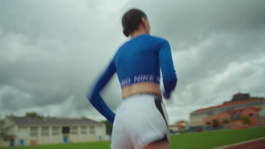 A close-up shot pans up from a female athlete's feet to her back as she sprints in slow motion on a red running track