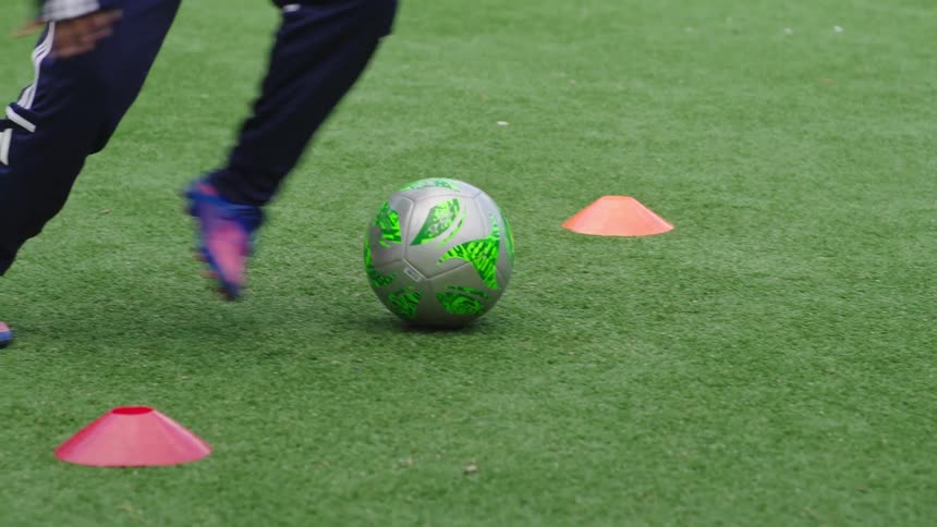 A close-up slow motion shot shows a soccer player's feet skillfully maneuvering a ball during training drills on an artificial turf field
