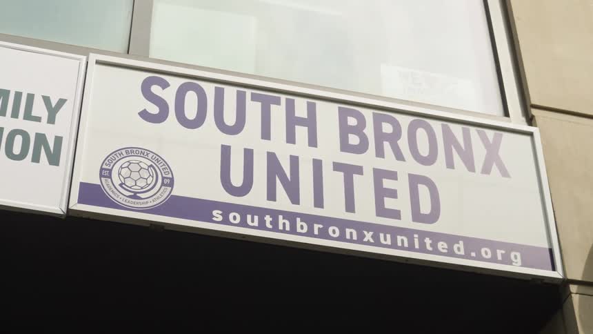 A low-angle establishing shot of the South Bronx United organization sign on a building