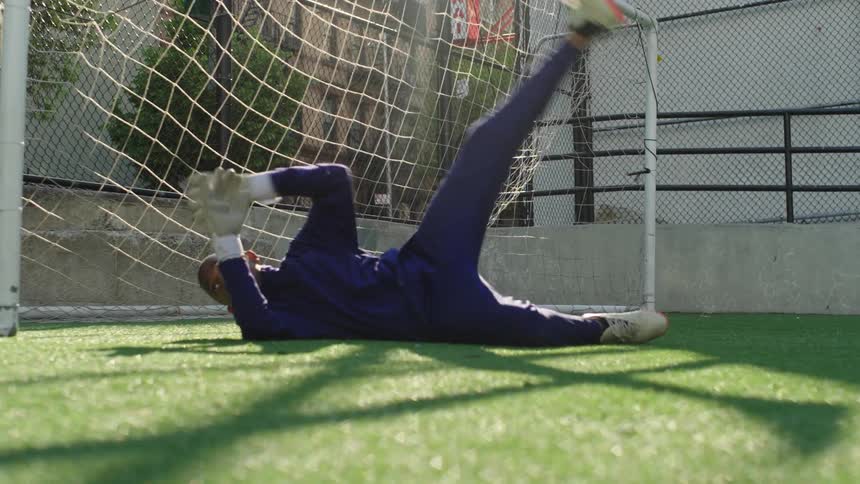 A young goalkeeper dives to make a save on a turf soccer field in slow motion