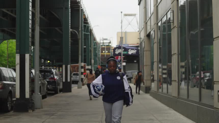 A young female athlete confidently walks down a city street with her soccer ball, listening to music on her headphones