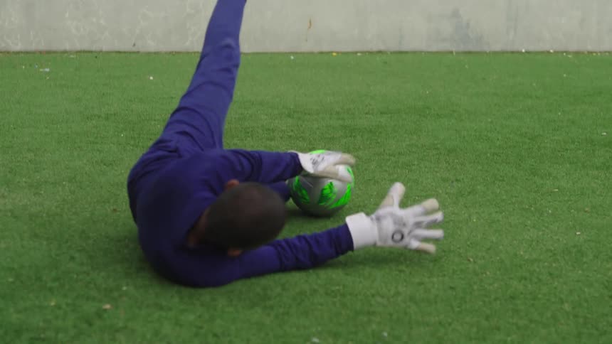 A young soccer goalie makes a great diving save on an artificial turf field in slow motion