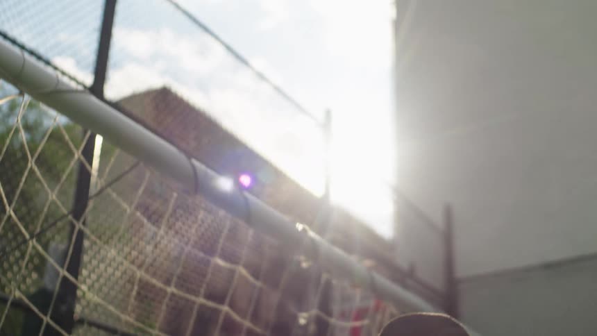 A determined young goalkeeper stands ready in front of a soccer goal, backlit by the bright sun in a slow-motion shot