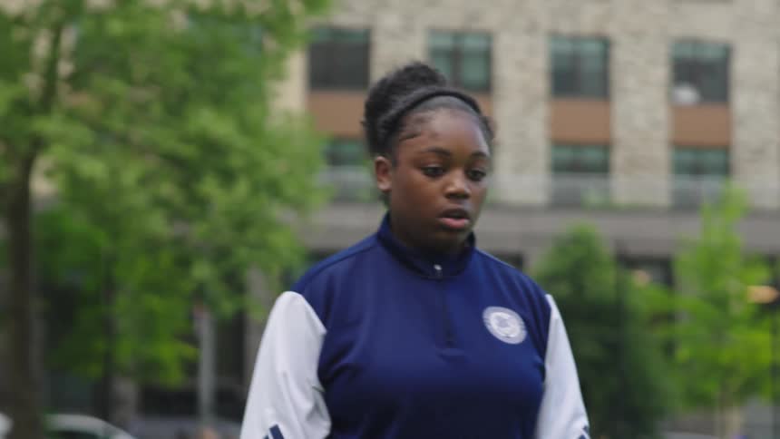 A young female athlete in a blue and white jacket warms up with footwork drills on an urban field in slow motion