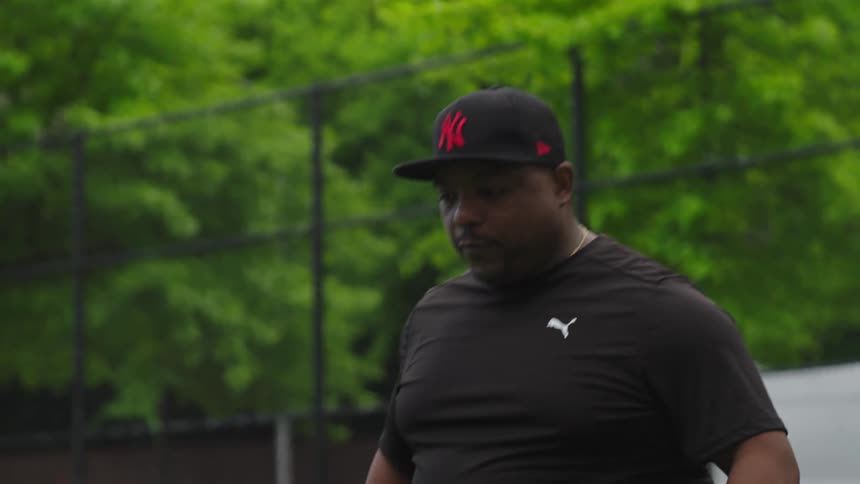 Slow motion shot of a focused African American coach wearing a Yankees cap during a practice session at an outdoor field