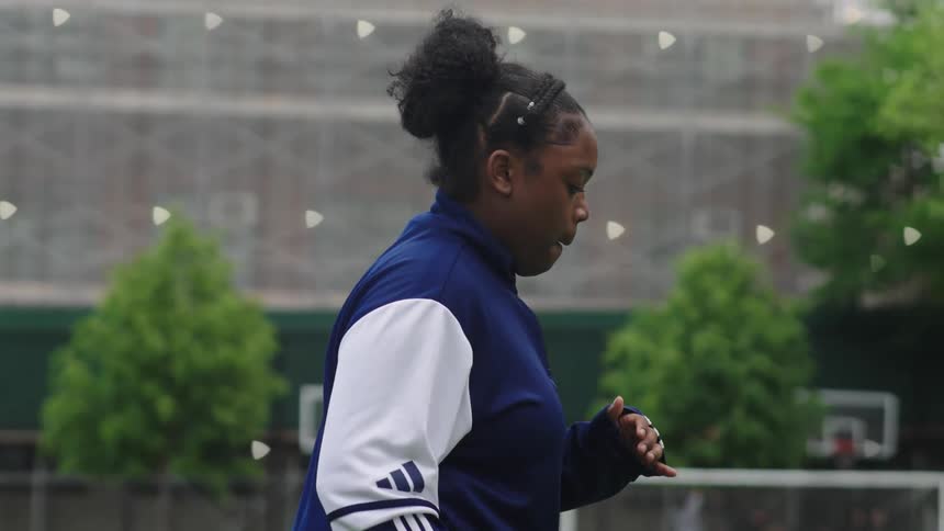 A determined young African American woman jogs in slow motion across a city sports field