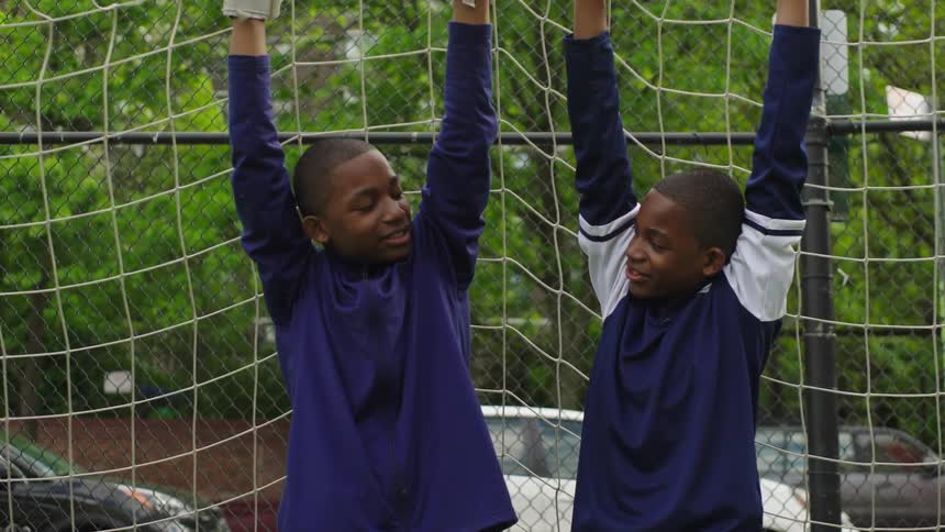 Two happy young boys playfully hang from a soccer goal crossbar and smile at each other in slow motion