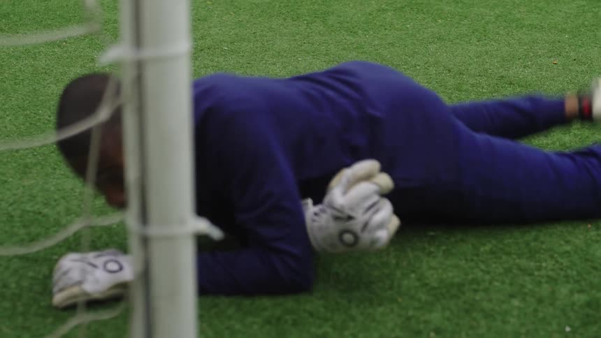 A young soccer goalie makes a spectacular diving save and gets back up in slow motion on an urban field