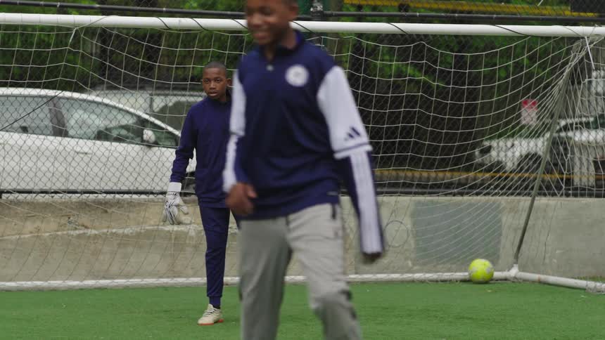A focused young boy in a goalkeeper uniform makes an incredible diving save during soccer practice on an urban field
