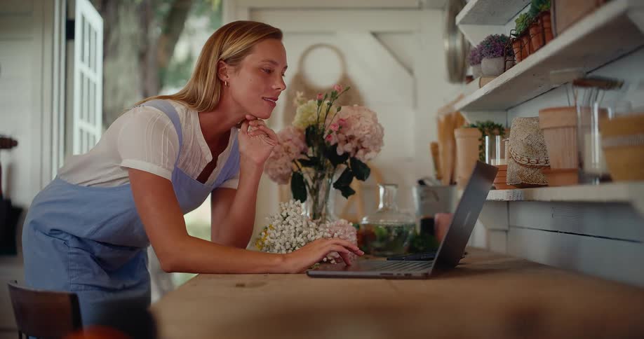 Cinemagraph of a thoughtful florist working on her laptop in a charming rustic workshop filled with flowers