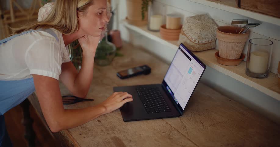 A focused female florist manages her small business on a laptop in her charming workshop