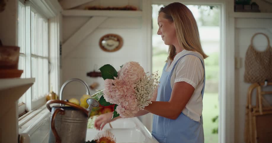 Happy young woman smelling and arranging a beautiful flower bouquet in a country house