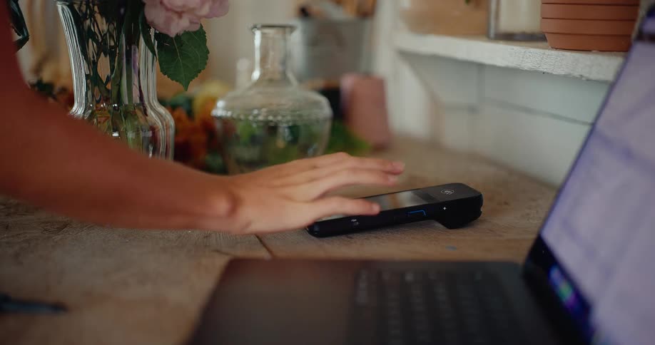 A woman works on her laptop and then uses a POS payment terminal to manage her small business transactions
