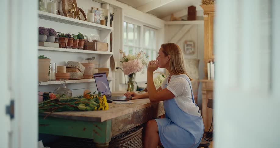A female florist manages her small business on a laptop from her charming and rustic flower workshop