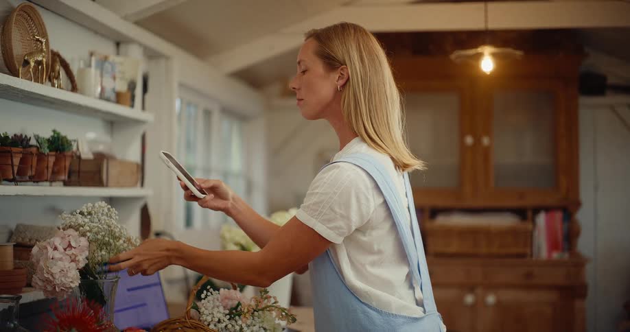 A female florist takes a photo of her beautiful flower arrangement on her smartphone in her charming, rustic workshop