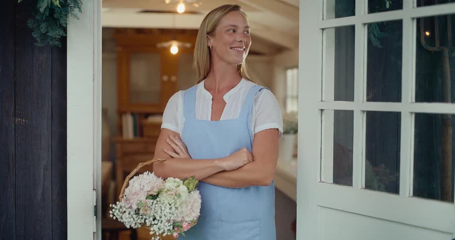 Proud female florist holding a basket of fresh flowers stands confidently in the doorway of her charming shop