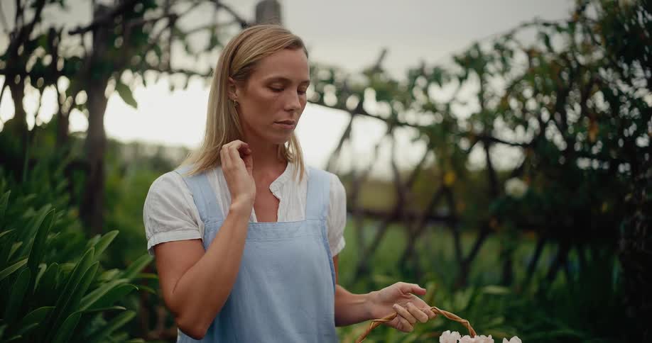 A serene woman in an apron holds a basket of fresh flowers and enjoys a peaceful moment in a lush garden