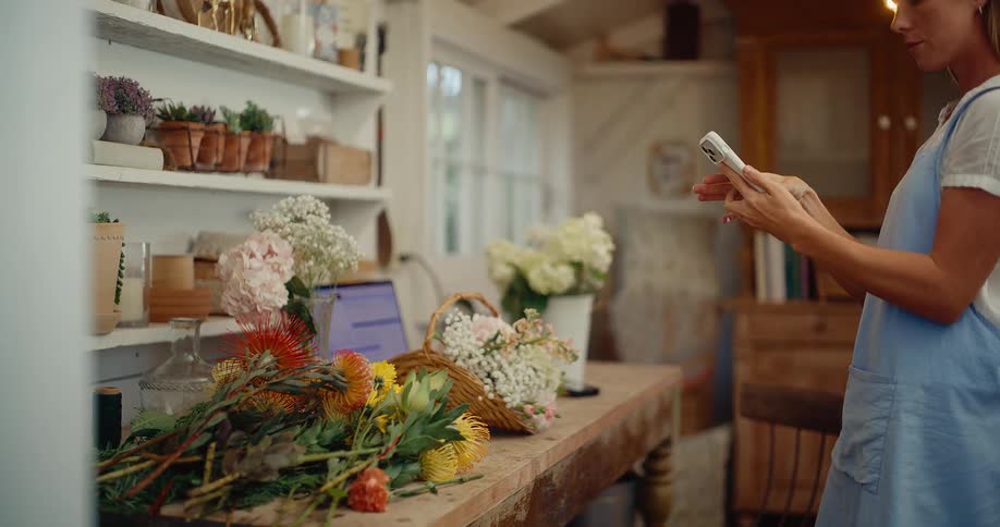Slow pull-back reveals a female florist taking a photo of her colorful flower arrangement in a rustic workshop