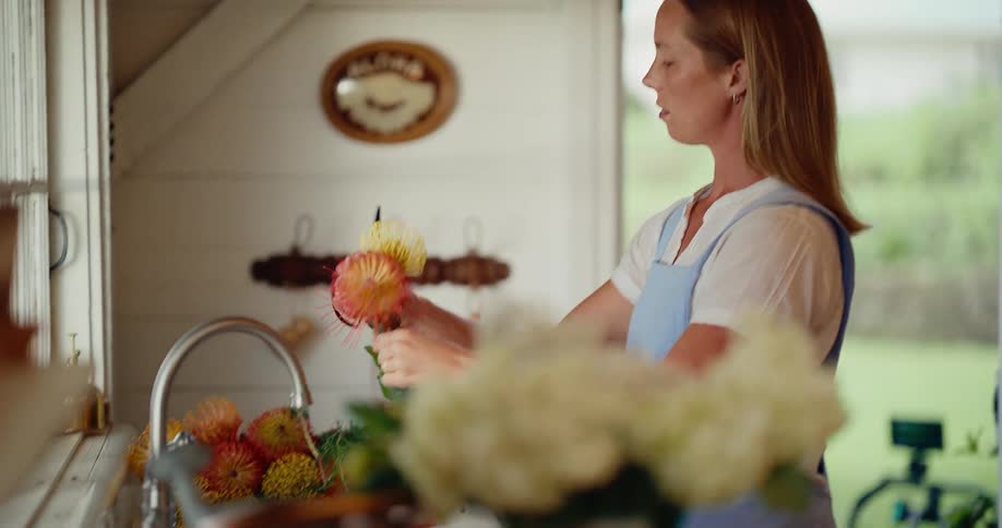 A woman in a rustic kitchen thoughtfully trims and arranges a vibrant bouquet of fresh flowers