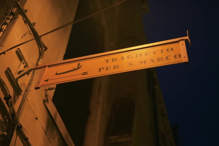 A classic Venetian sign points the way to the Traghetto gondola ferry for St. Mark's Square at night
