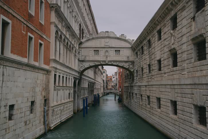A static wide shot of the iconic Bridge of Sighs spanning a canal between historic buildings in Venice, Italy on a cloudy day