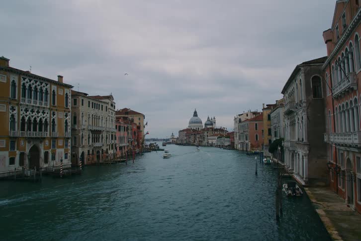 A wide shot of the Grand Canal in Venice, Italy, with boats navigating the waters past historic buildings under a cloudy sky