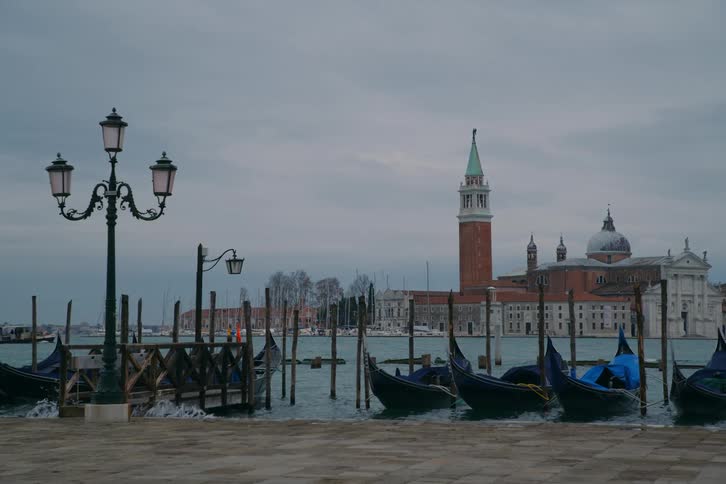 Moored gondolas sway on the choppy waters of the Venetian lagoon with the Church of San Giorgio Maggiore visible on a cloudy day