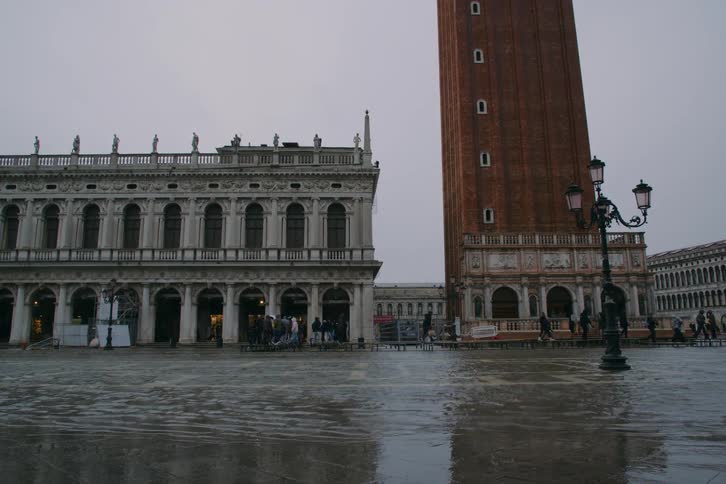 St. Mark's Square in Venice is flooded with water as people walk by the Campanile on an overcast day