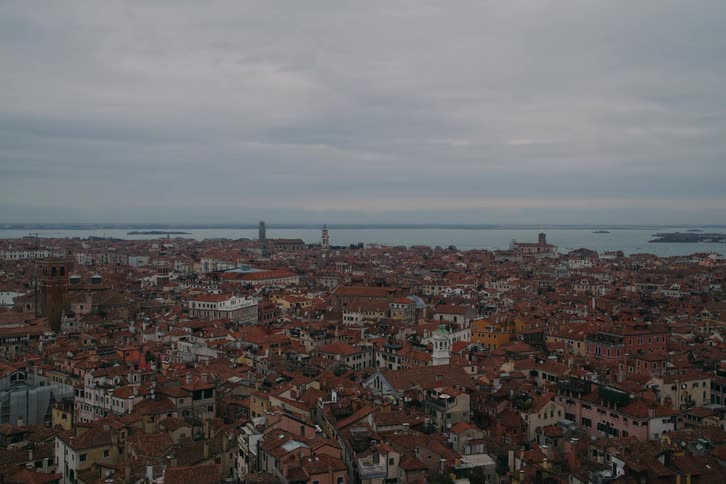 A panoramic cityscape of Venice, Italy, showcasing the dense, historic red rooftops under a moody, overcast sky