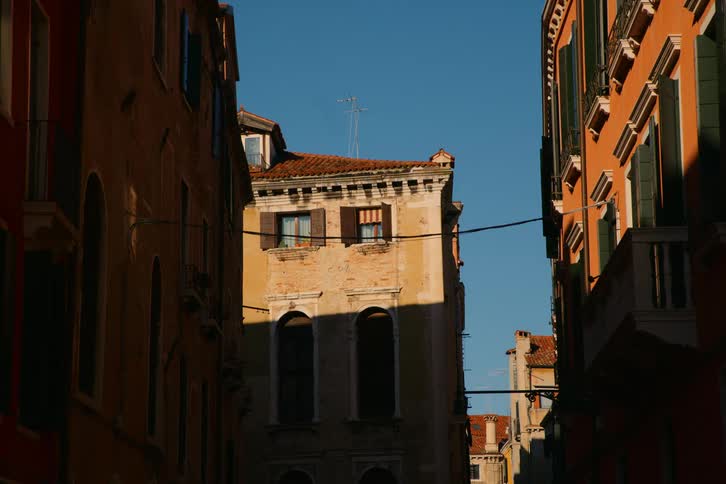 A classic Venetian building bathed in sunlight stands between two shadowy buildings against a clear blue sky