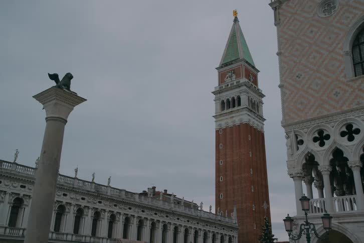 A low-angle view of the iconic St. Mark's Campanile bell tower in Venice, Italy, standing tall against a gloomy, overcast sky