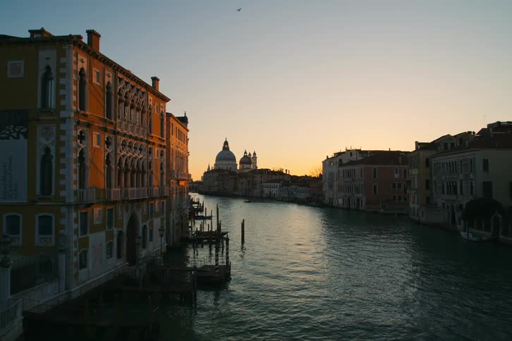The tranquil Grand Canal in Venice is bathed in the warm golden light of sunrise, with the Basilica di Santa Maria della Salute in the distance
