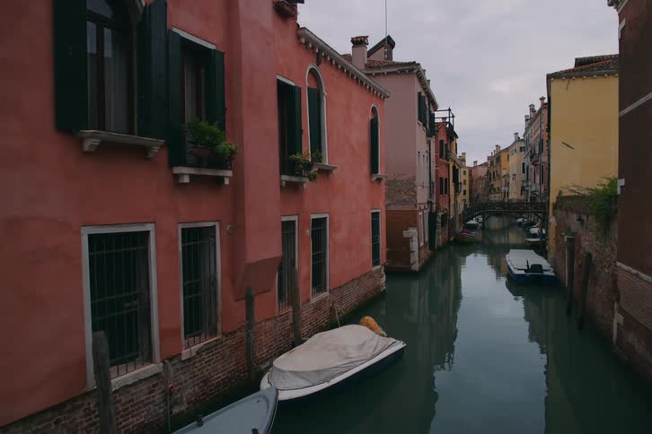 A serene canal flows between colorful historic buildings in Venice, Italy, on a cloudy day