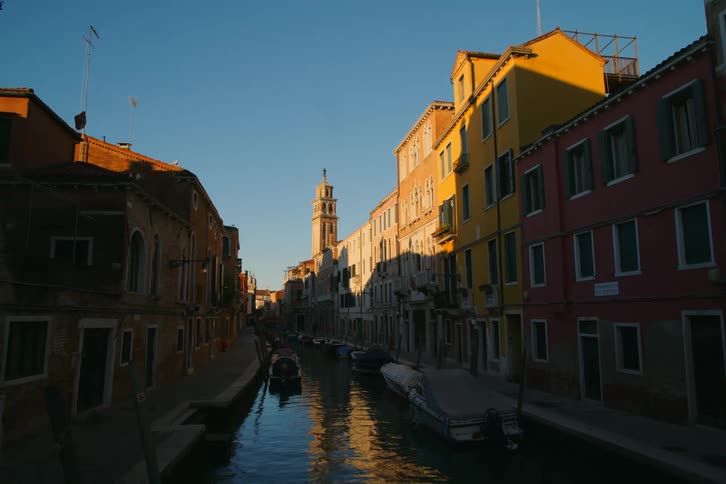 Golden hour light shines on the colorful buildings along a peaceful canal in Venice, Italy