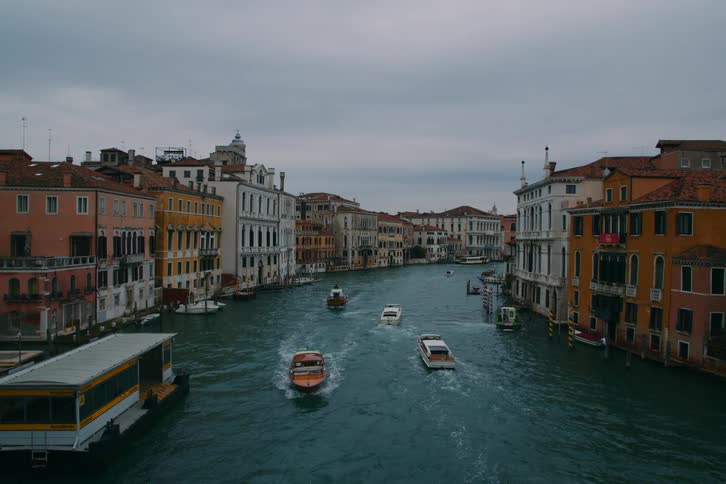 Water taxis and public transport boats travel down the iconic Grand Canal in Venice, Italy, on a cloudy day
