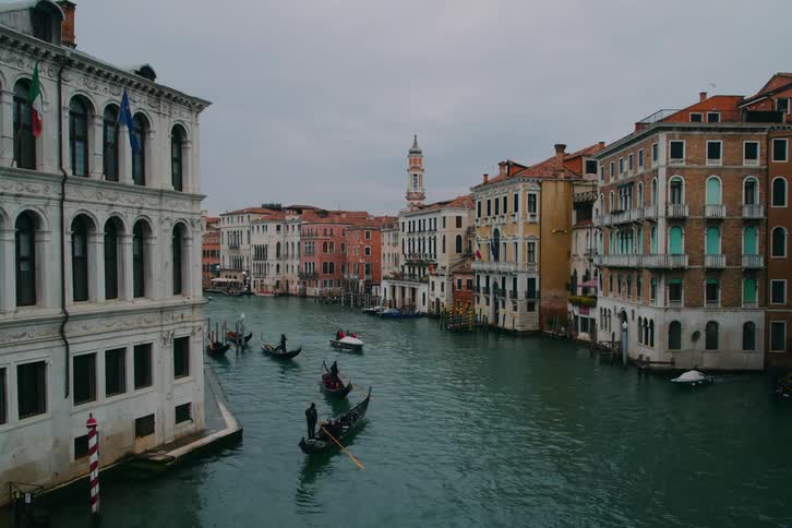 Gondolas drift along the famous Grand Canal in Venice, Italy, surrounded by historic buildings on an overcast day
