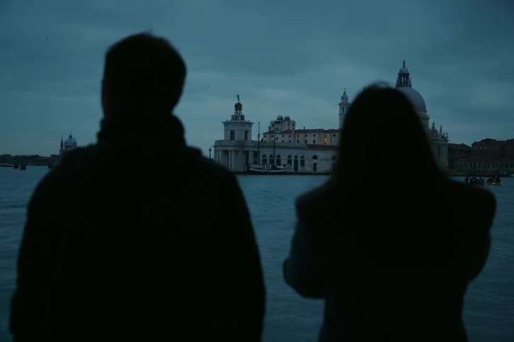 A silhouetted couple gazes at the Basilica di Santa Maria della Salute across the Grand Canal during a moody blue hour in Venice, Italy