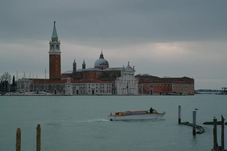 A water taxi crosses the Venetian Lagoon in front of the historic Church of San Giorgio Maggiore on a cloudy day in Venice, Italy
